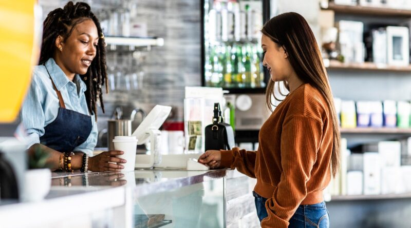 Young woman using credit card reader at coffee shop counter