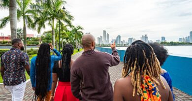 Local Tour Guide Walking and Pointing Toward the Skyline with a Group of Cheerful, Fashionable Afro-Descendant Tourists Together with a View of Panama City