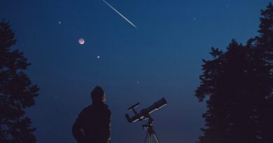 Silhouette of a man, telescope, stars, planets and shooting star under the night sky.