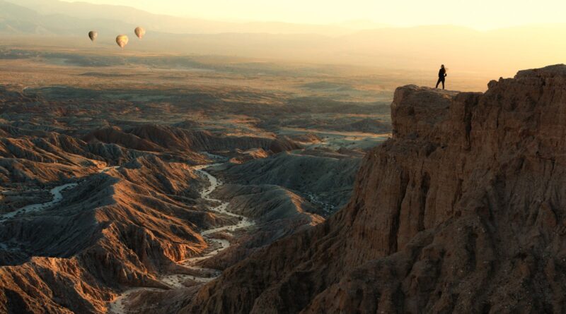 Woman standing on Font's Point looking at hot air balloons flying over badlands, Anza-Borrego Desert State Park, California, USA